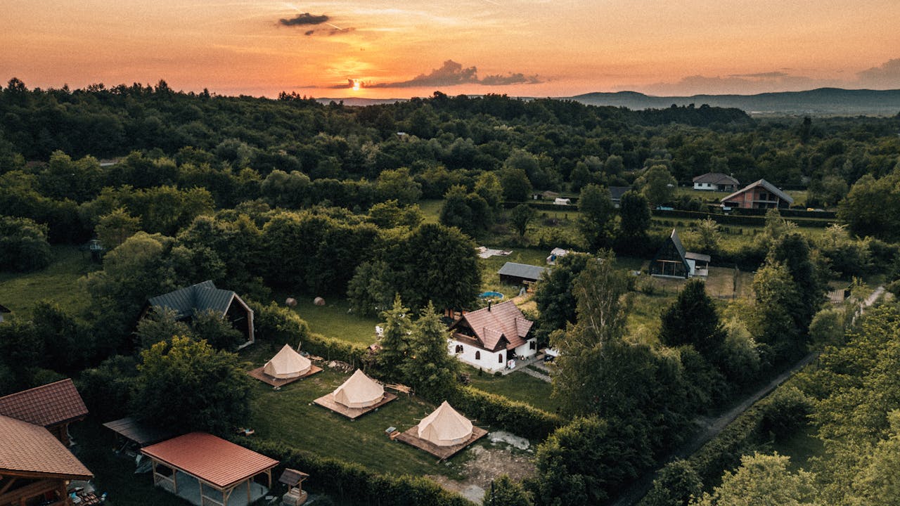 Crafting Captivating Headlines: Your awesome post title goes here Aerial view of Romania's lush countryside with tents and homes at sunset.